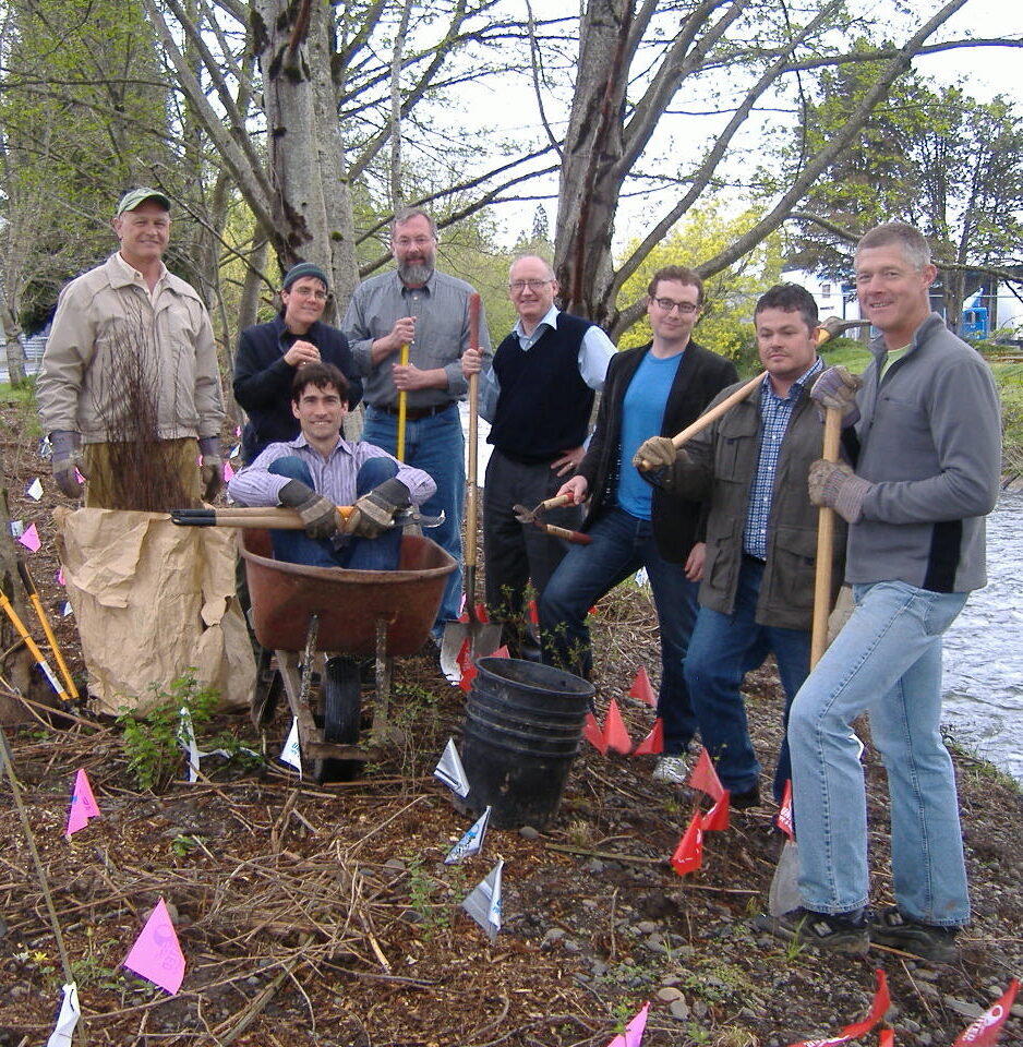 members of board of directors standing as a group near Johnson Creek - one is sitting in a wheelbarrow