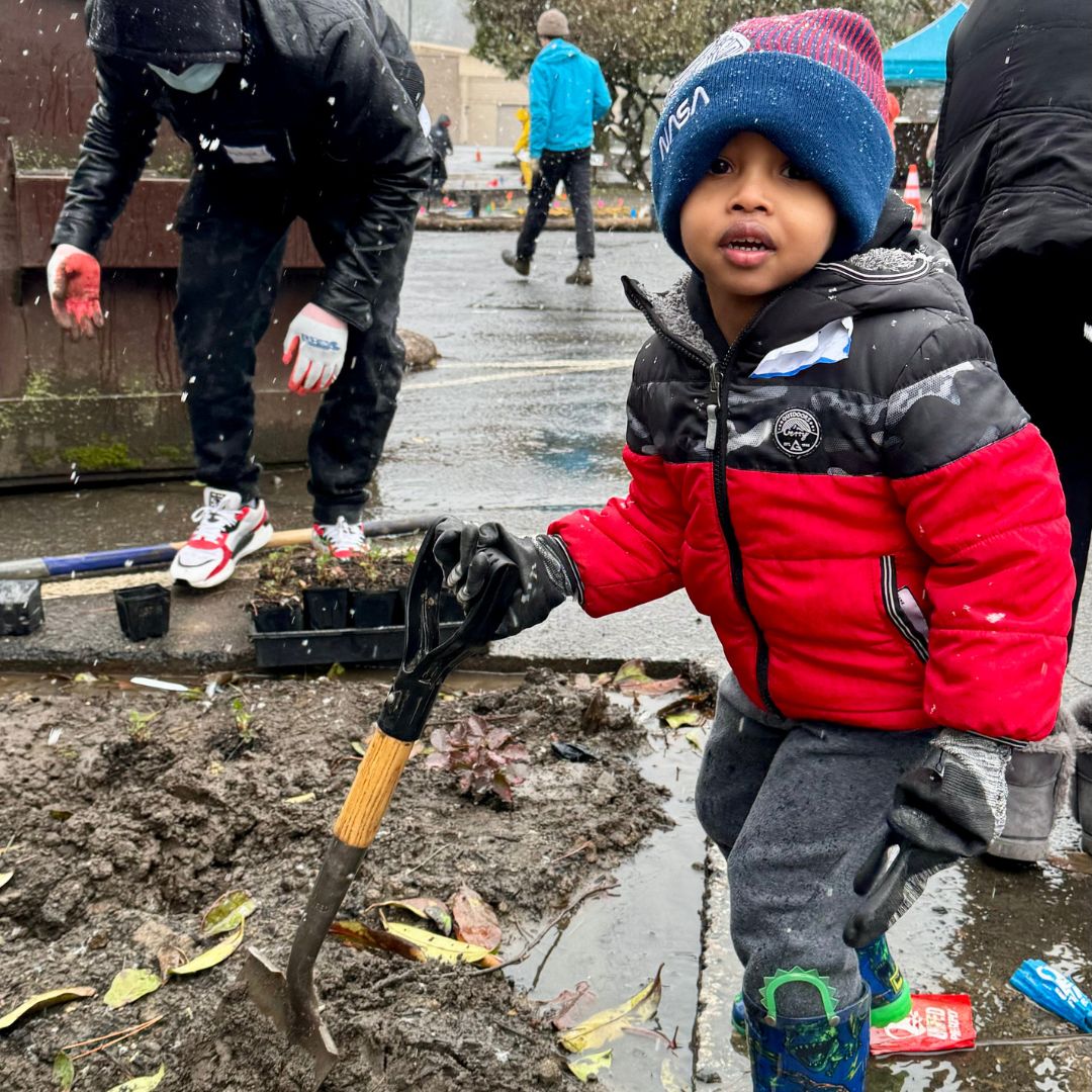 A child holds a small shovel to plant native plants in a rain garden. 