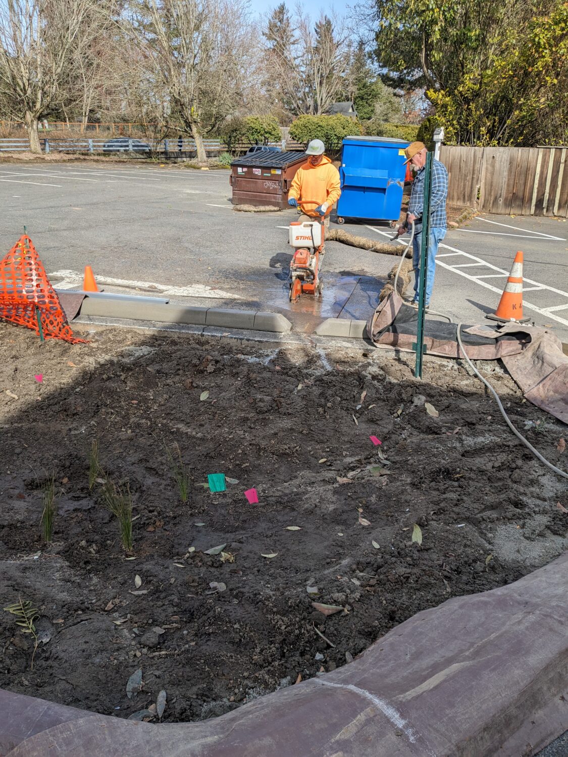 Contractors saw cutting pavement in a parking lot to install a trench drain, which will drain into a rain garden.
